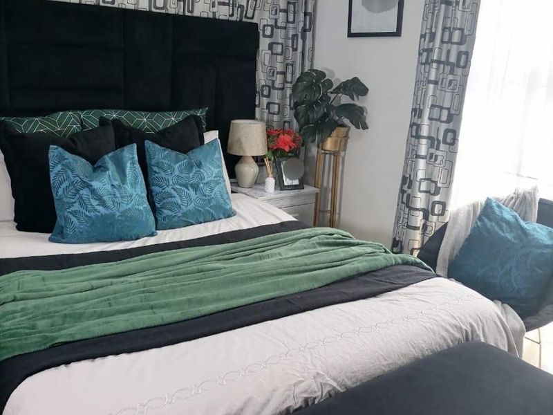 A well-lit bedroom featuring a large upholstered headboard and floor-to-ceiling patterned curtains.