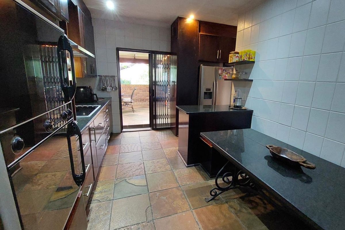 A functional kitchen featuring dark cabinetry, granite countertops, a built-in oven, and natural stone flooring with direct access to an outdoor patio area.