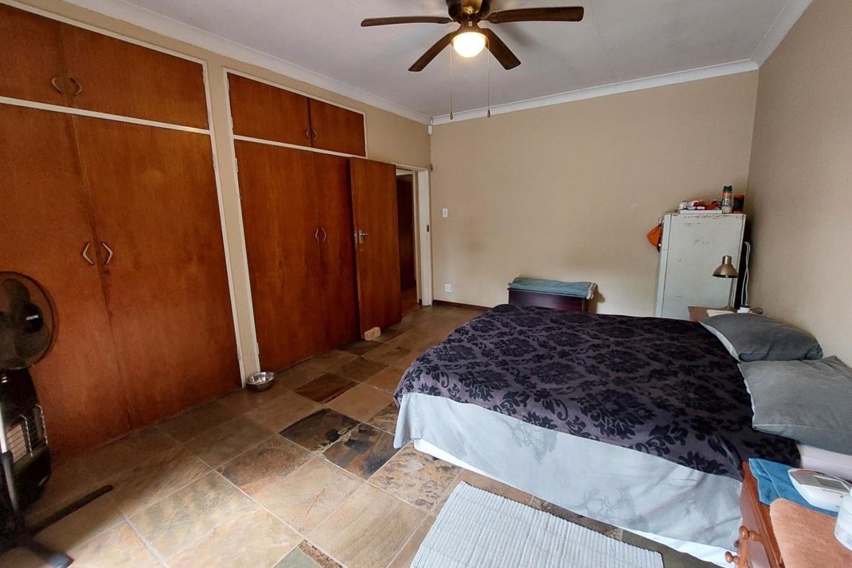 A bedroom featuring built-in wooden cupboards, tiled flooring, and a ceiling fan.