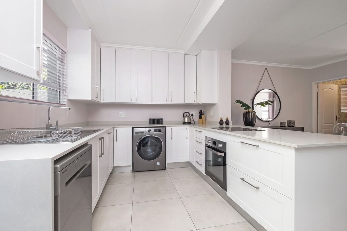 Modern kitchen featuring white cabinetry, stone countertops, integrated oven, hob, and space for a washing machine, finished with neutral floor tiles.