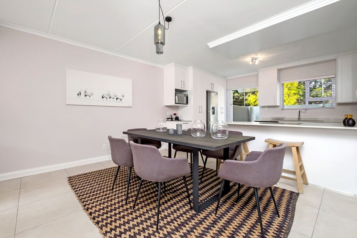 Open-plan dining area seamlessly connected to a modern kitchen featuring white cabinetry, stone countertops, and a breakfast bar.