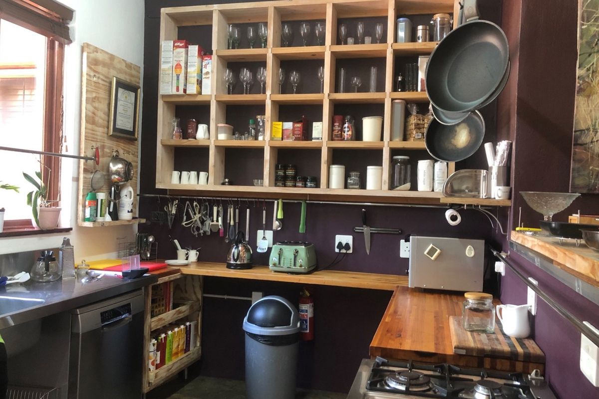A functional kitchen area featuring open timber shelving, dark accent walls, stainless steel countertops, and a built-in gas hob.