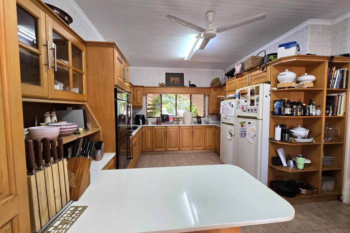 A functional kitchen featuring extensive wooden cabinetry, built-in oven, tiled flooring, and a central breakfast bar area with ample storage space.