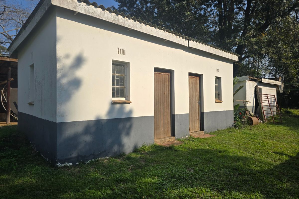 A detached outbuilding on the farm property featuring a corrugated roof, timber doors, and steel-framed windows, set within a grassy garden area.
