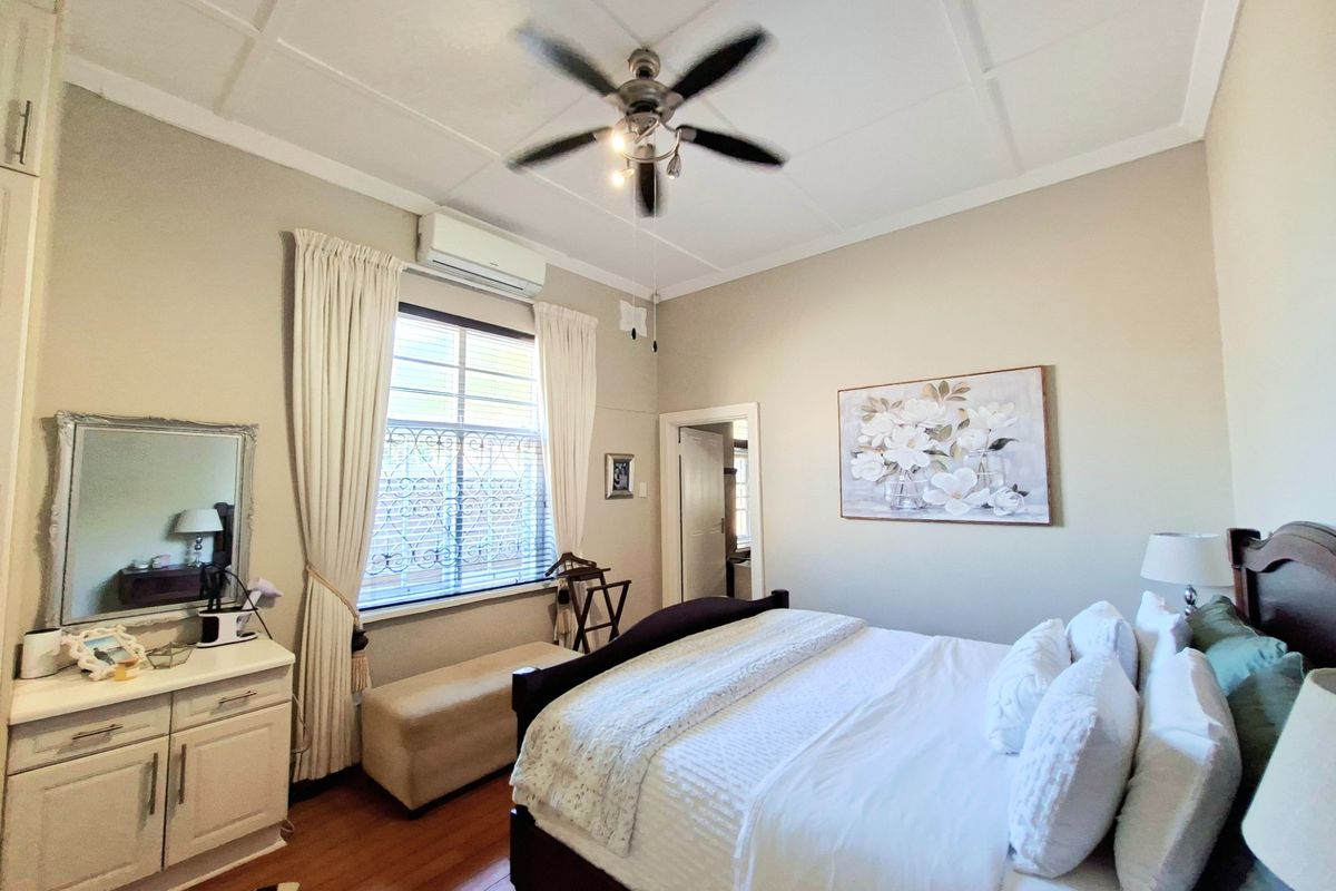 A well-maintained bedroom featuring high ceilings, a ceiling fan, and a wall-mounted air conditioning unit, providing a comfortable and functional living space.