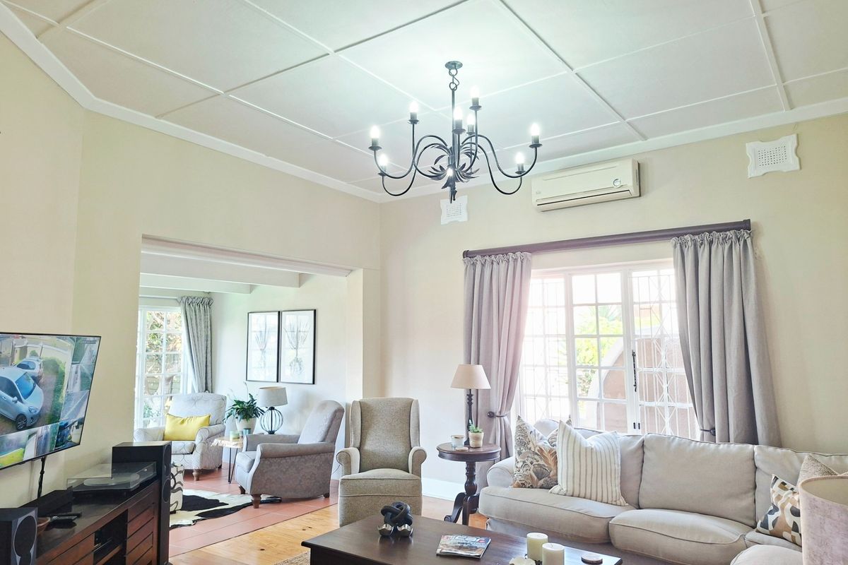 Spacious living room featuring polished timber flooring, a decorative ceiling, and a wall-mounted air conditioning unit, flowing into an adjacent seating area.