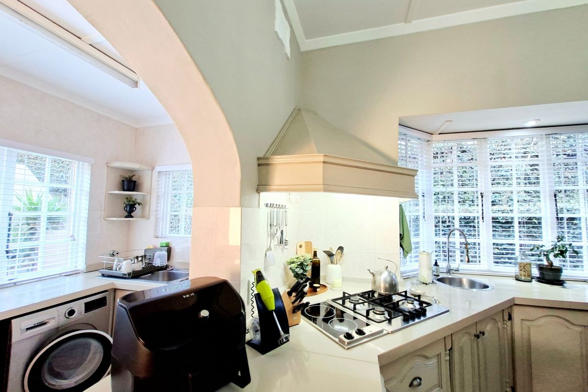 A bright kitchen featuring a gas hob, extractor fan, integrated sink, and built-in cabinetry, with an adjoining laundry area visible through an arched opening.