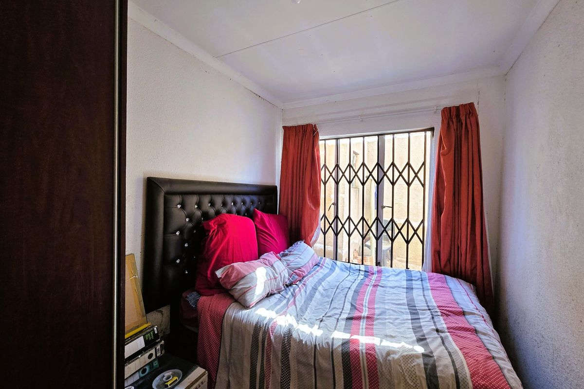 A compact bedroom featuring a built-in wardrobe and a window secured with metal security bars.