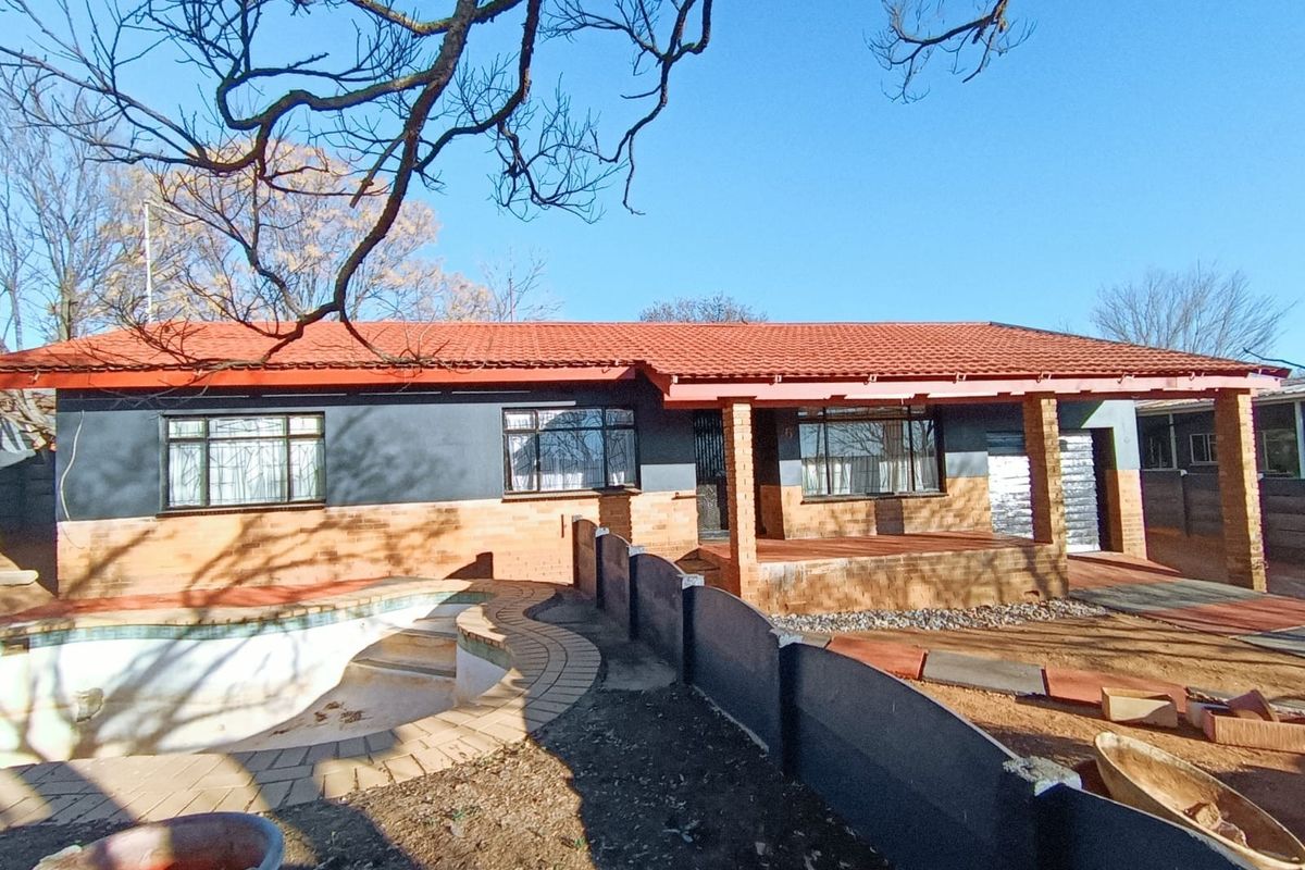 Rear view of a single-story house featuring a tiled roof, brick facade, covered patio, and an empty swimming pool in the backyard.