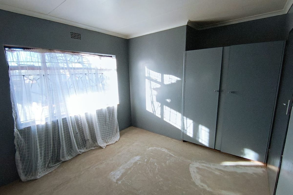 An empty bedroom featuring a built-in wardrobe, security bars on the window, and worn flooring in need of refurbishment.