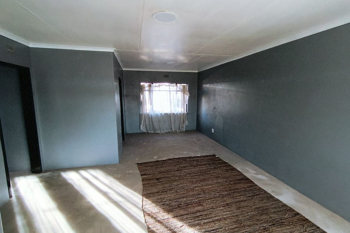 An empty living room featuring dark grey painted walls, recessed ceiling lighting, and a window, providing a blank canvas for interior design.