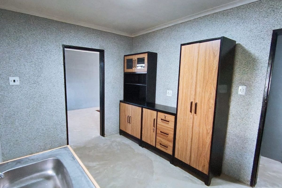 A functional kitchen area featuring built-in wooden cabinetry, a stainless steel sink, and textured wall finishes, currently awaiting final flooring installation.