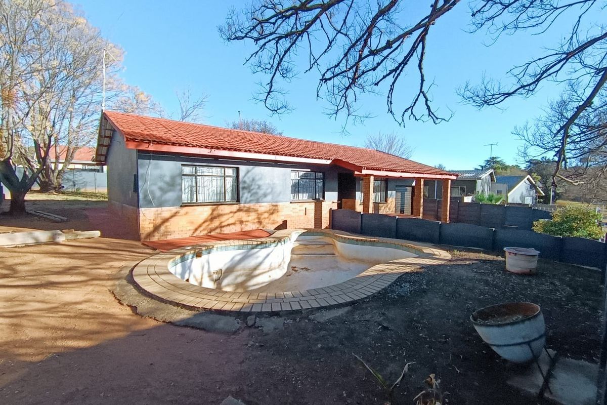 Rear view of the house featuring a swimming pool, covered patio, and brick and painted exterior walls set in an unlandscaped garden.