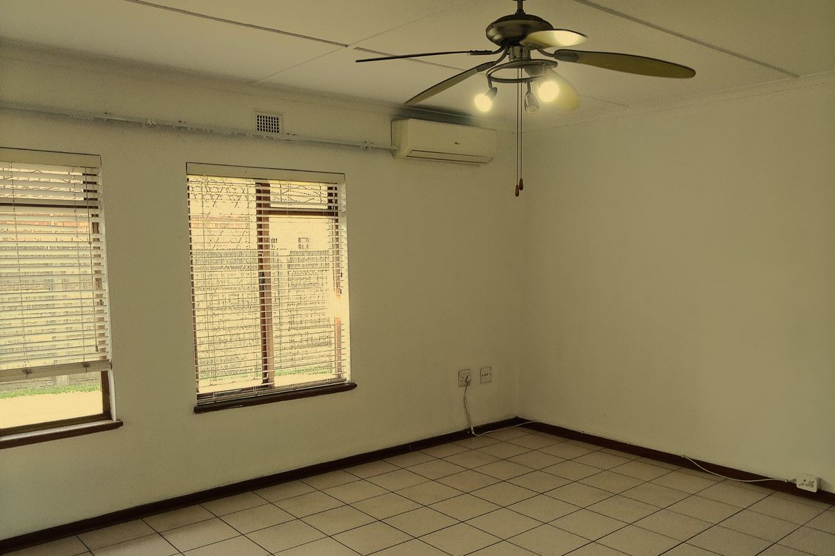An empty living room featuring tiled flooring, a ceiling fan, and a wall-mounted air conditioning unit.