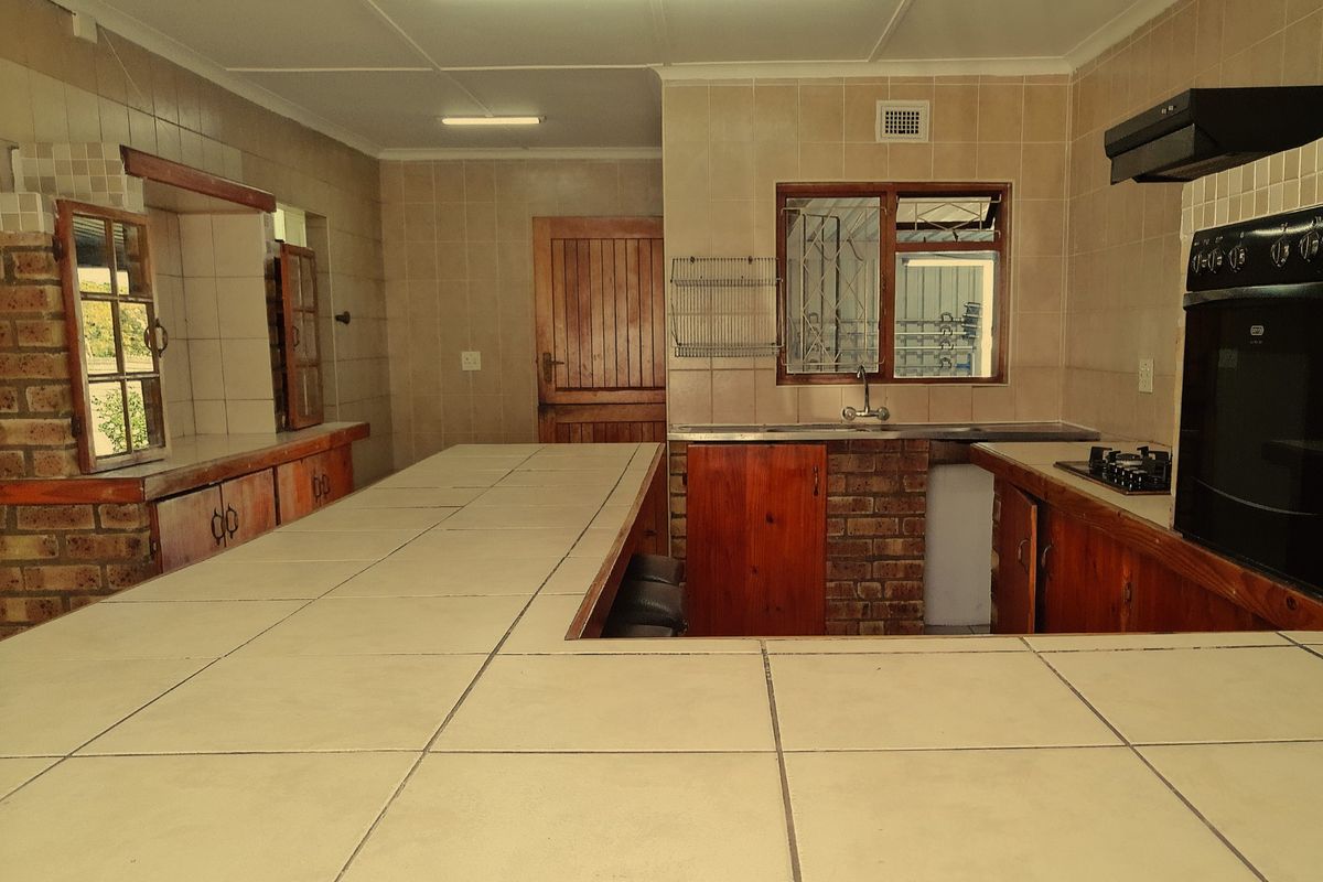 A dated kitchen featuring brick-base cabinetry, tiled countertops, and a built-in oven with extractor fan, offering a functional layout with significant renovation potential.