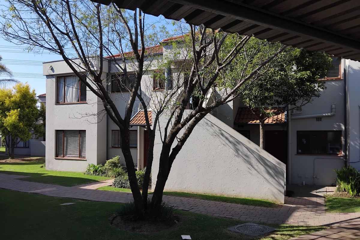 Exterior view of a multi-story apartment complex featuring paved walkways, landscaped garden areas, and a covered entrance pathway.
