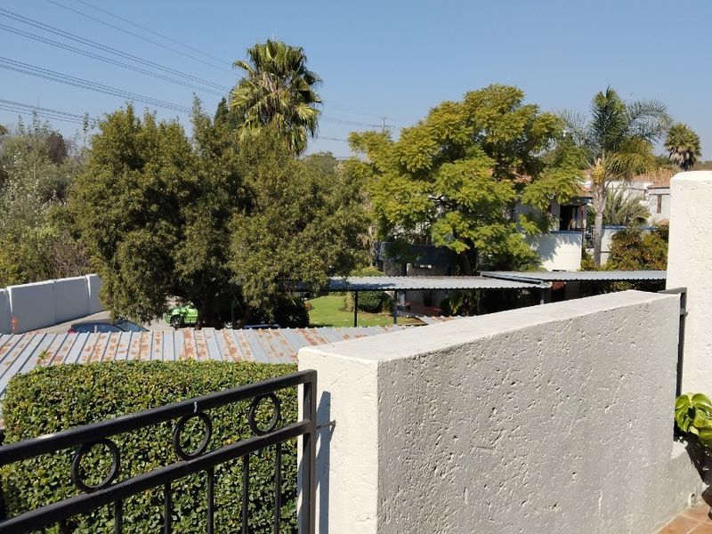 A balcony with a metal railing and tiled flooring, offering an elevated view of the surrounding neighborhood and mature trees.