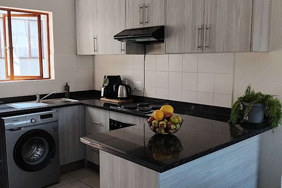 A functional kitchen featuring light wood-grain cabinetry, dark granite countertops, a built-in extractor fan, and integrated space for a washing machine.