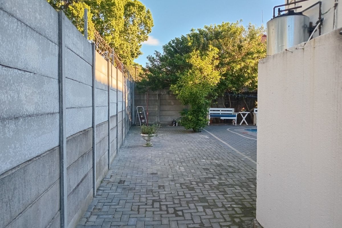 A paved side walkway leading to a rear garden area, featuring precast concrete boundary walls and an external water heater unit.
