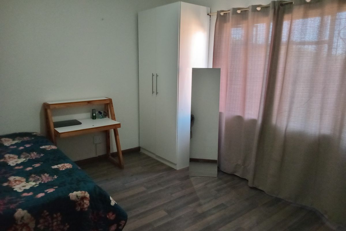 A bedroom featuring wood-look laminate flooring, a built-in white wardrobe, and a window with curtain treatments.