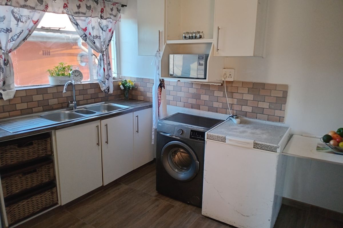 Functional kitchen featuring white cabinetry, a double stainless steel sink, tiled backsplash, and dedicated space for laundry appliances.