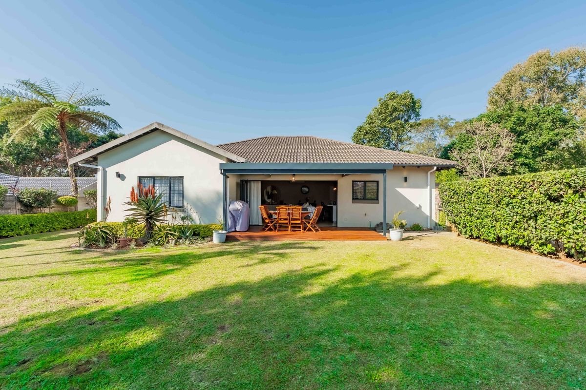 Rear view of the townhouse featuring a covered patio with timber decking, overlooking a well-maintained private garden and lawn area.