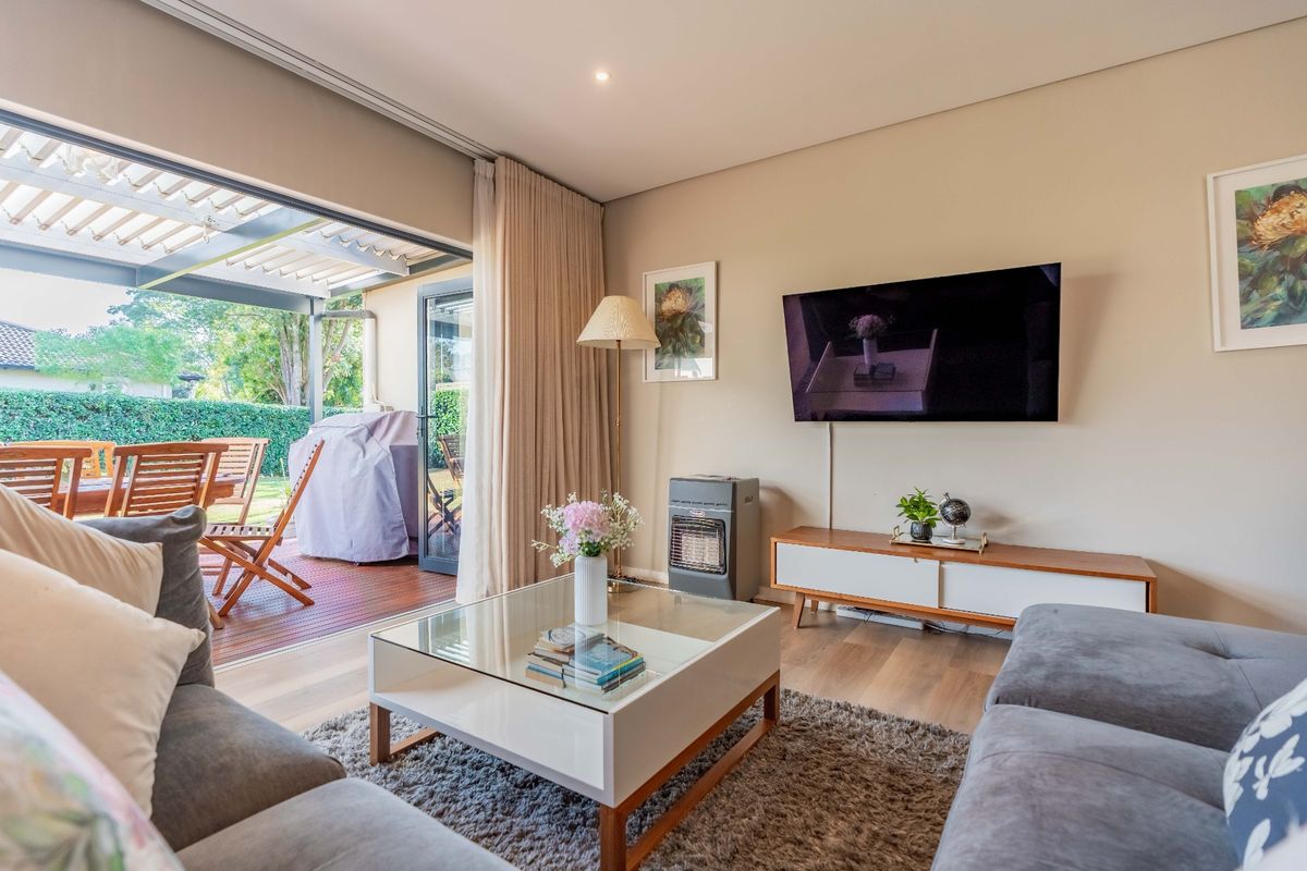 A bright living room featuring wood-look flooring and large sliding doors that open onto a covered patio area.