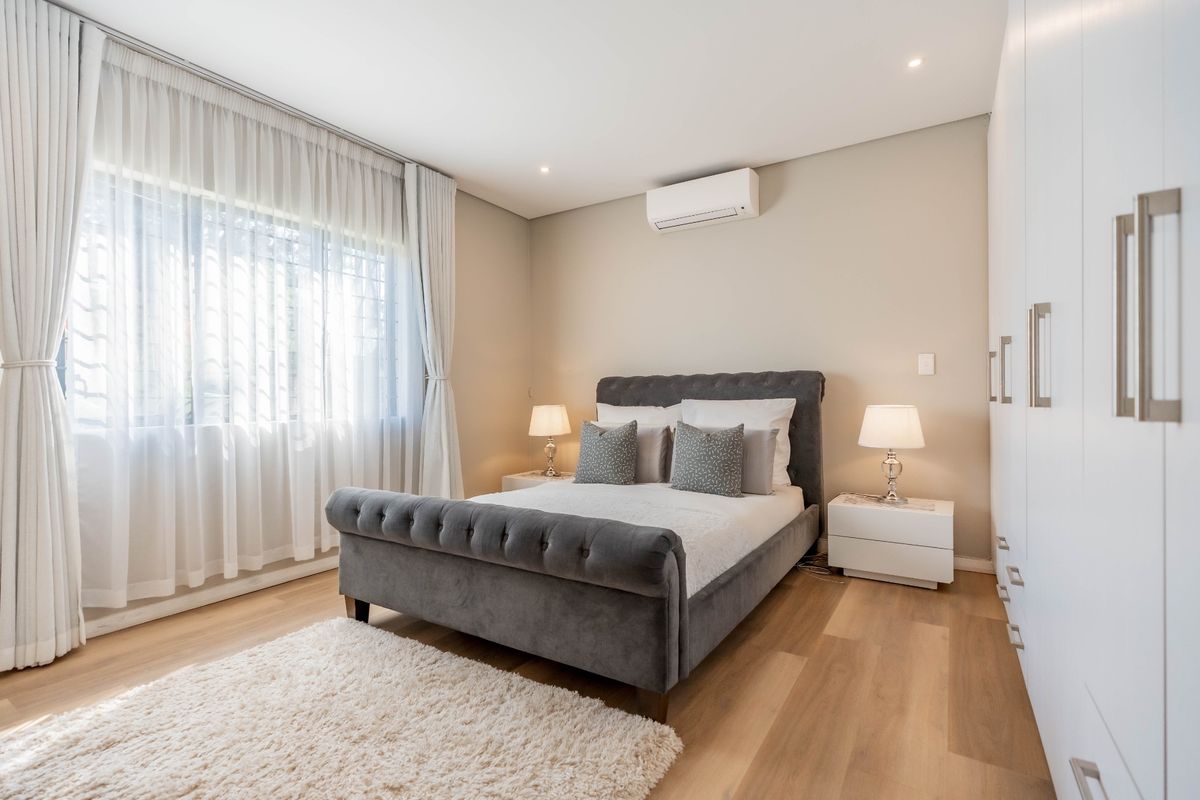 A well-maintained bedroom featuring light wood-look flooring, built-in floor-to-ceiling wardrobes, recessed downlighting, and a wall-mounted air conditioning unit.