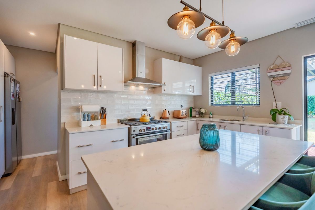 Modern kitchen featuring white cabinetry, stone countertops, a central island, stainless steel gas stove with extractor fan, and subway tile backsplash.