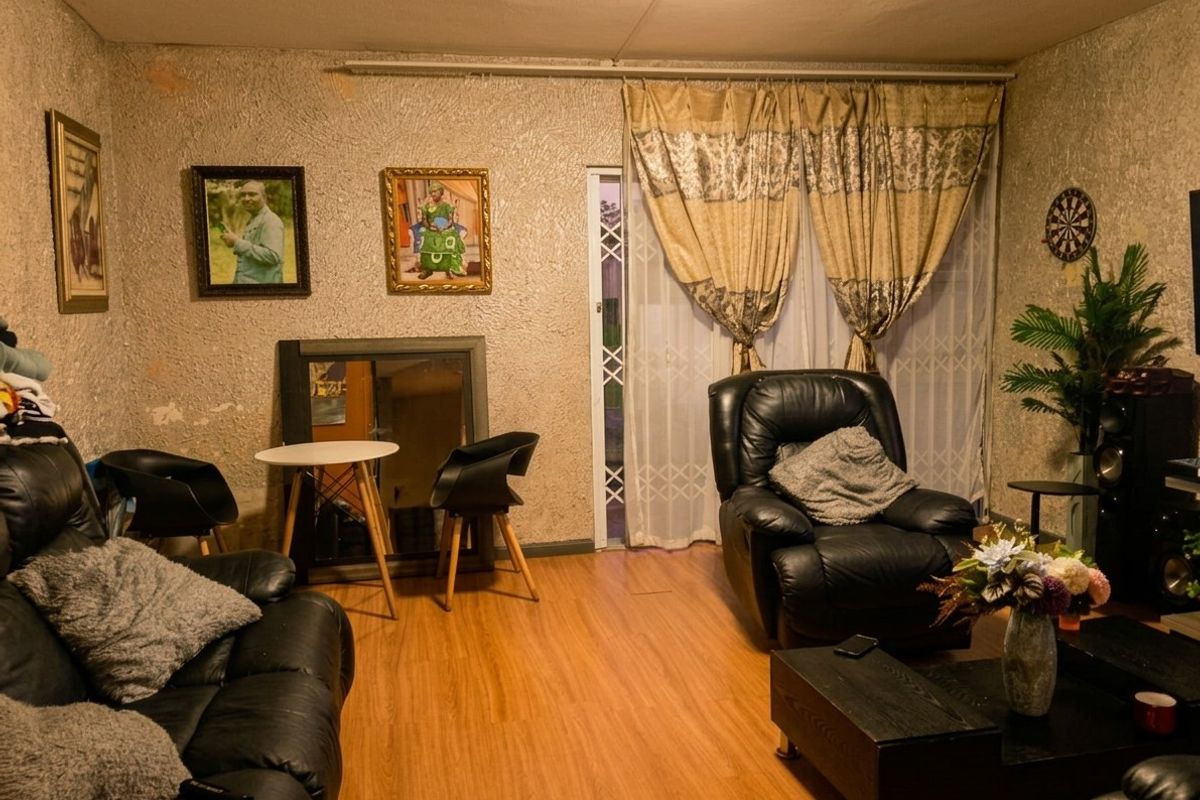 A living room featuring wood-look laminate flooring and a sliding glass door with security gate, providing access to the exterior.
