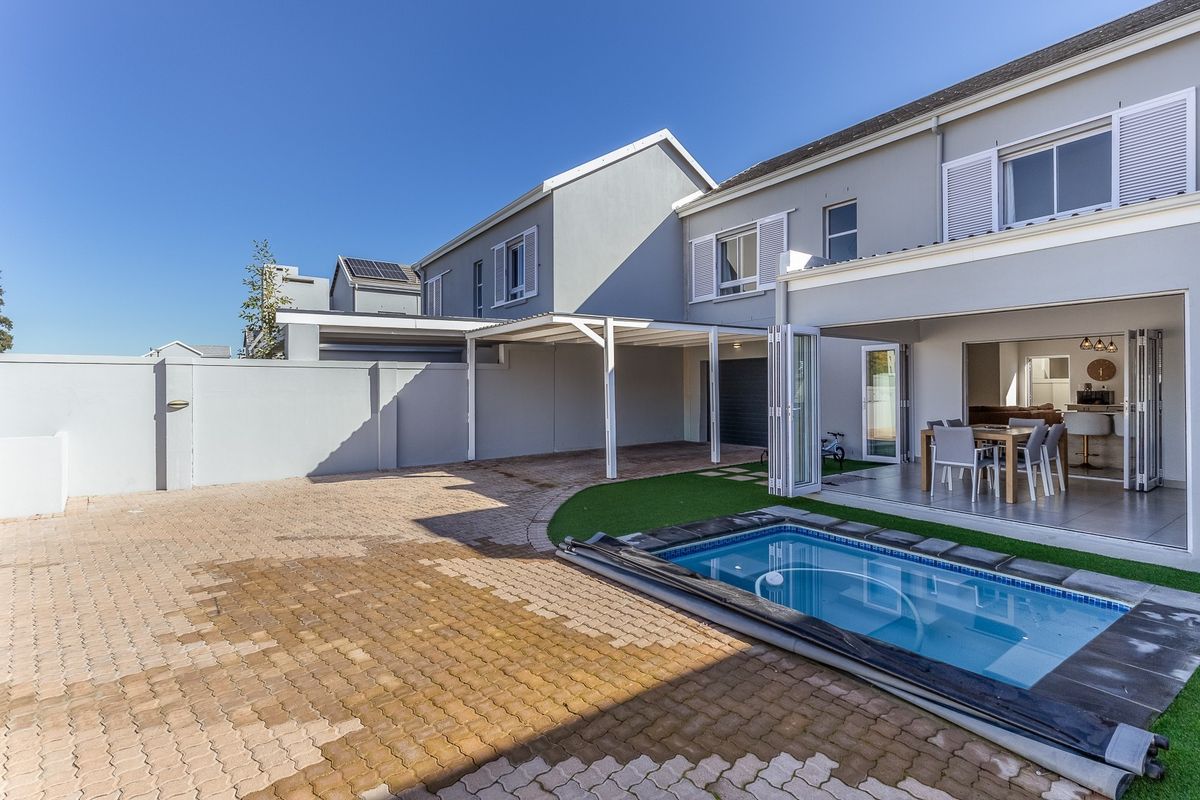 Rear view of the property featuring a paved courtyard, covered patio, swimming pool, and direct access to the open-plan living area.