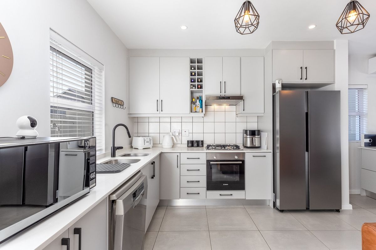 Modern kitchen featuring light grey cabinetry, tiled backsplash, built-in oven, gas hob, extractor fan, and sleek stone countertops.