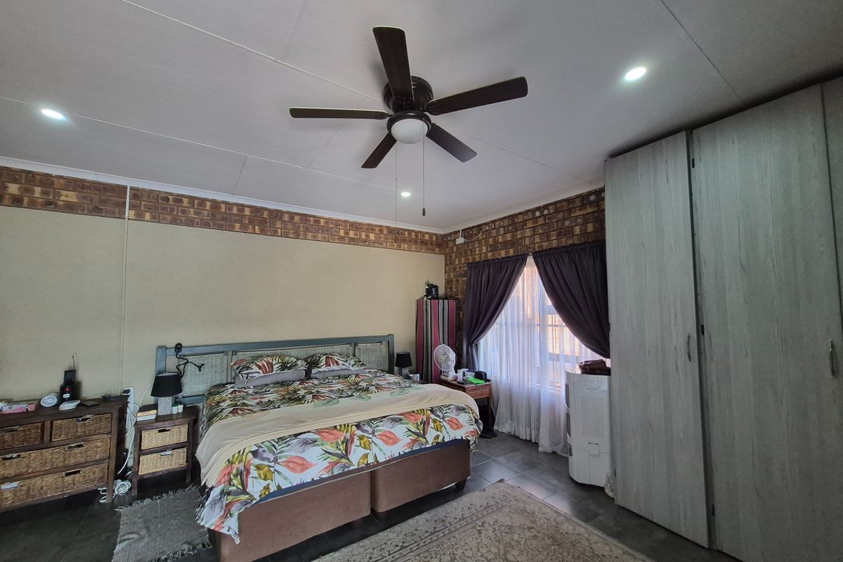 Spacious bedroom featuring a ceiling fan, built-in cupboards, and a decorative brickwork accent wall.