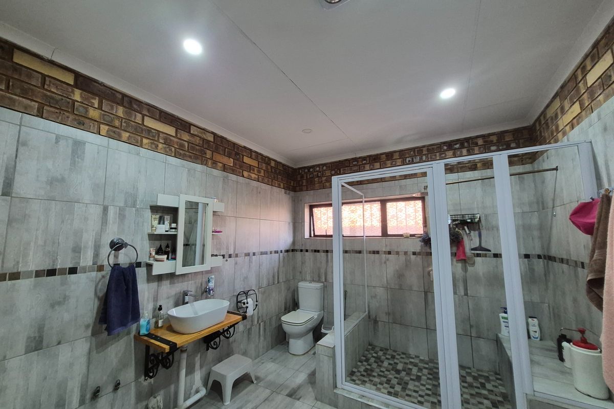 A bathroom featuring a vessel sink on a wooden vanity, a walk-in shower with glass enclosure, and tiled walls with a decorative brick border.