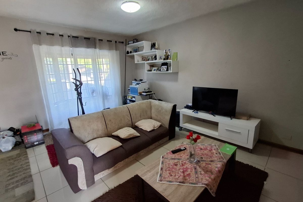A comfortable living room featuring tiled flooring, large sliding glass doors providing natural light, and wall-mounted shelving units.