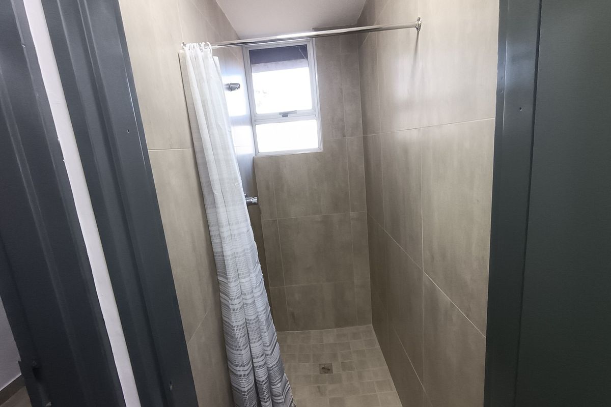 A functional shower stall featuring neutral wall tiling, a built-in shower head, and a window for natural light.