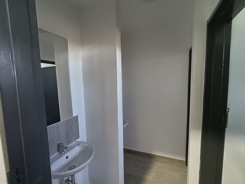 A clean, modern bathroom featuring a wall-mounted basin, mirror, and neutral flooring, presenting a functional and well-maintained space.