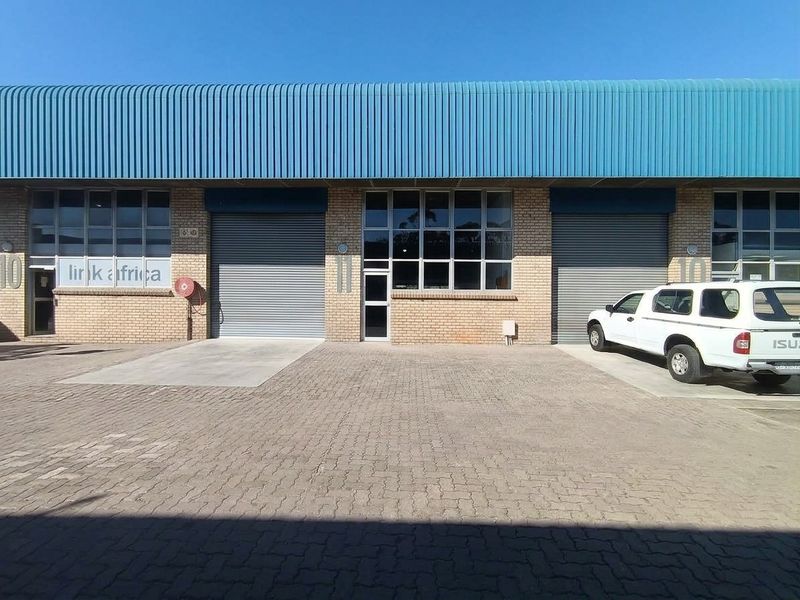 Commercial warehouse exterior featuring brick facade, roller shutter doors, and paved driveway access.