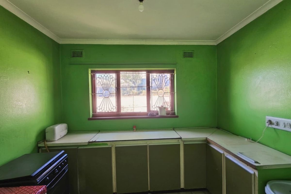 A dated kitchen featuring original cabinetry, laminate countertops, and security bars on the window, offering a blank canvas for a modern renovation.