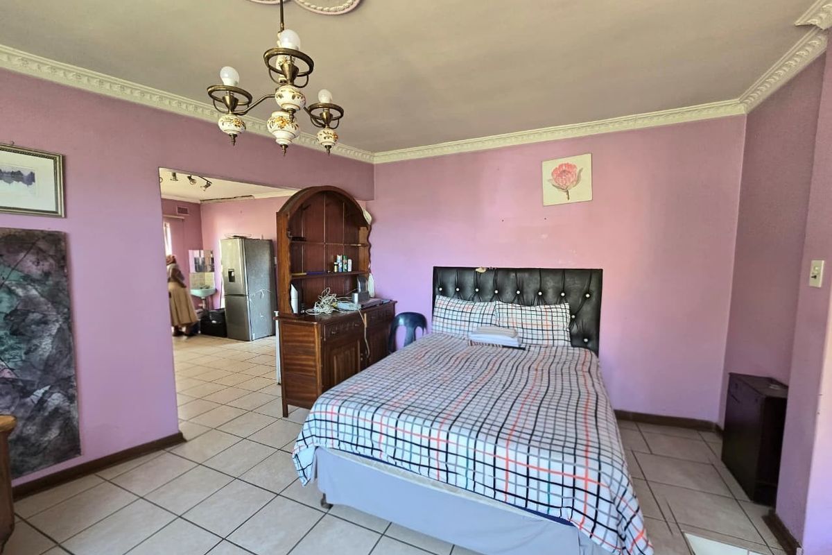 A bedroom featuring tiled flooring, decorative ceiling cornicing, and a central chandelier, with an open-plan transition into an adjacent utility area.