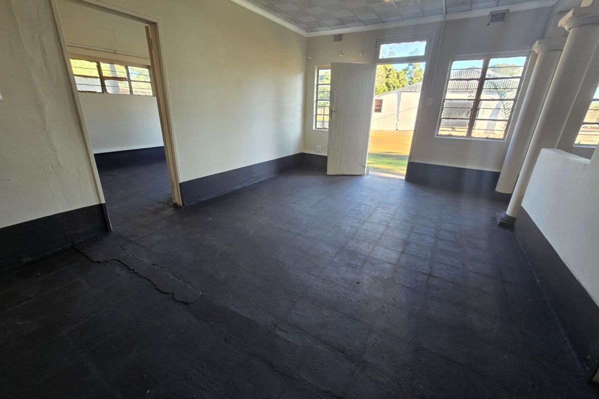 An empty interior room featuring dark painted tiled flooring, a drop ceiling, and direct access to an outdoor area through a single door.