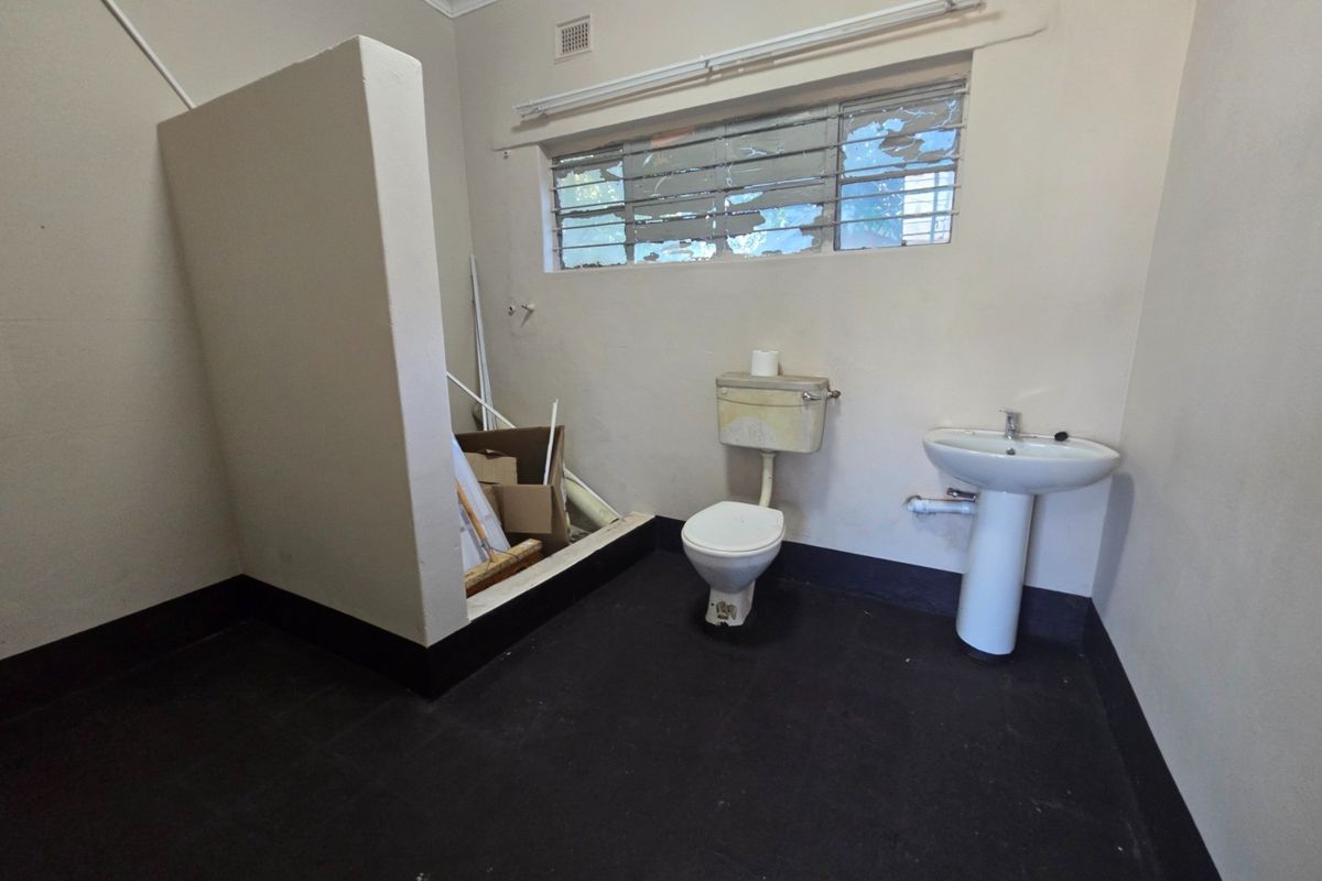 A basic commercial restroom featuring a pedestal basin, toilet, and partitioned area, requiring significant maintenance and cosmetic updates.