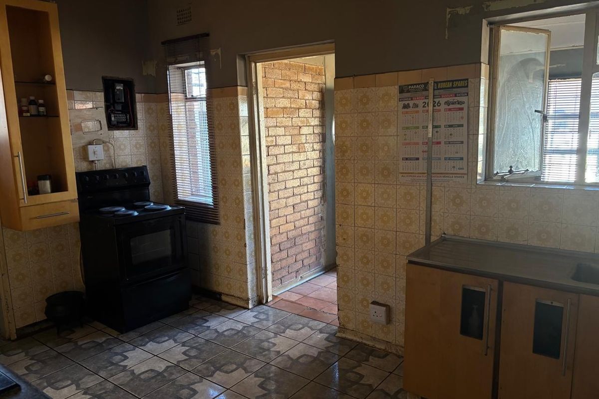 A dated kitchen featuring original wall tiles, built-in cabinetry, and a freestanding stove, offering significant potential for a modern renovation.