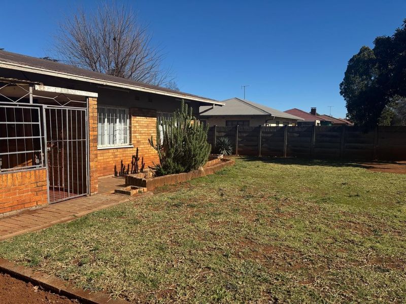 A view of the rear garden featuring a brick facade, a paved patio area, and a perimeter boundary wall.