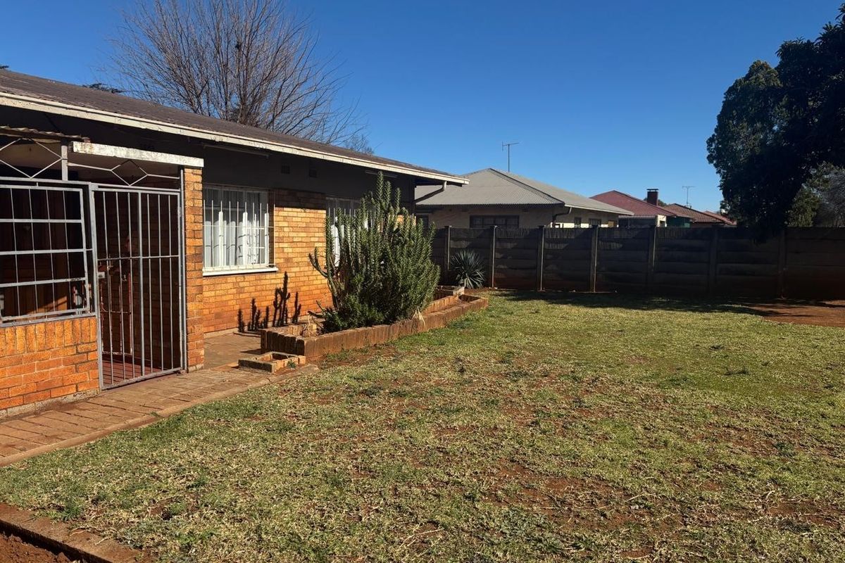 A view of the rear garden featuring a brick facade, a paved patio area, and a perimeter boundary wall.