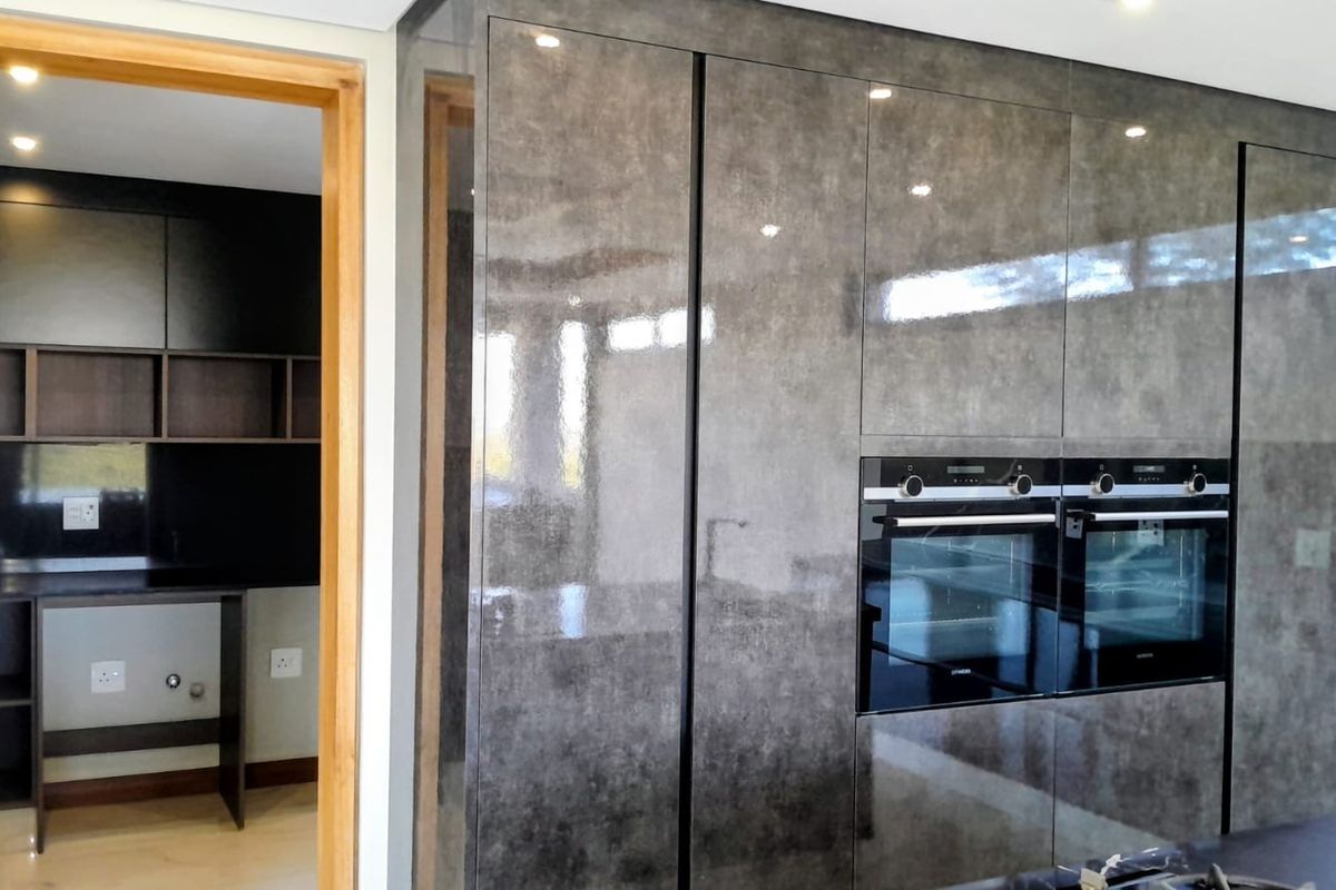 Modern kitchen featuring high-gloss cabinetry, integrated double ovens, and an adjacent scullery area with built-in shelving and workspace.