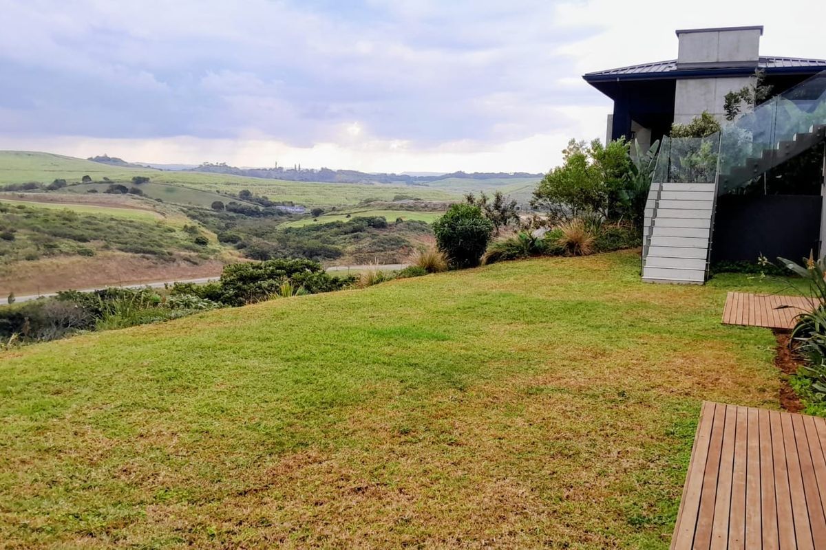 A spacious rear garden featuring a wooden deck, glass-railed staircase, and expansive views of the surrounding rolling hills and landscape.
