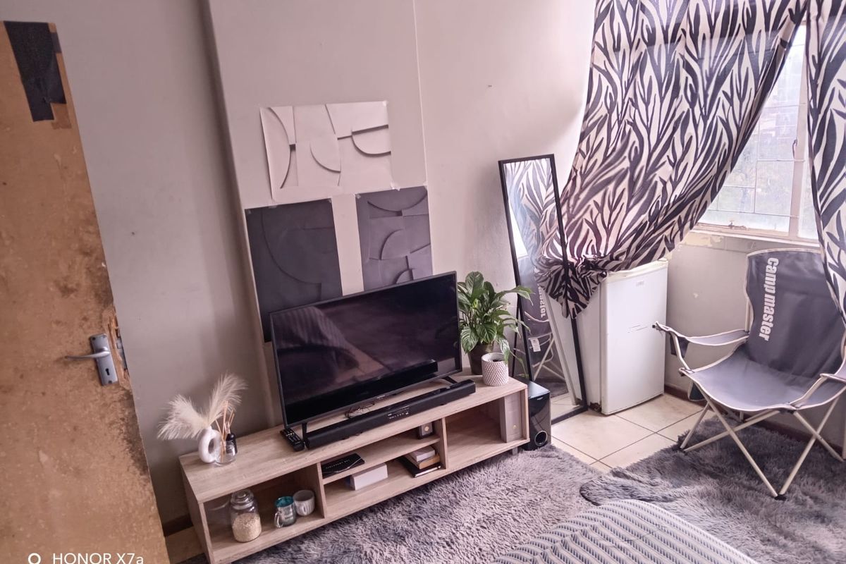 A living area featuring tiled flooring, a window with patterned curtains, and a built-in wall section, showing signs of wear on the door frame.