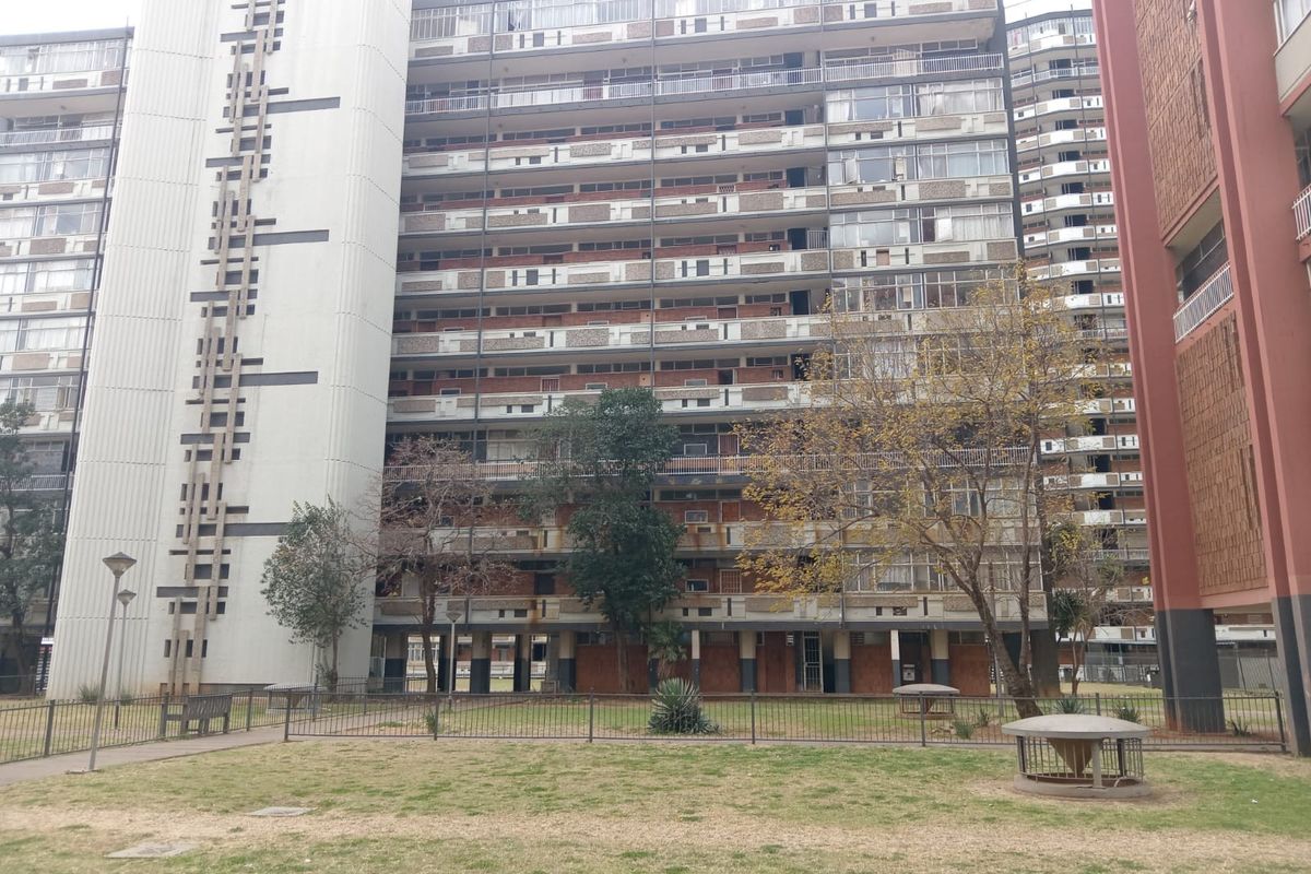 Exterior view of a large multi-story apartment complex featuring a central courtyard area with established trees and lawn.