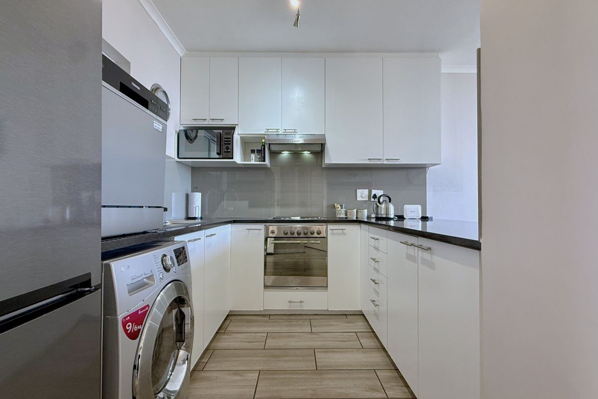 Modern U-shaped kitchen featuring white cabinetry, dark stone countertops, integrated oven, extractor fan, and tiled flooring.